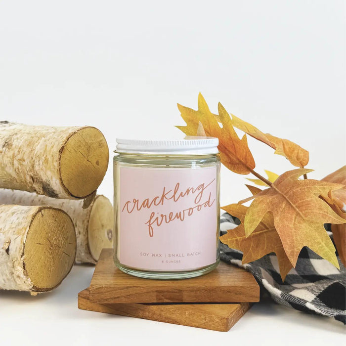 “Amber glass candle labeled CRACKLING FIREWOOD surrounded by pinecones and holiday décor.”

“Hand-poured soy candle burning beside a cozy fireplace and mug of cocoa.”

“Flat lay of CRACKLING FIREWOOD candle with matchsticks and festive greenery.”